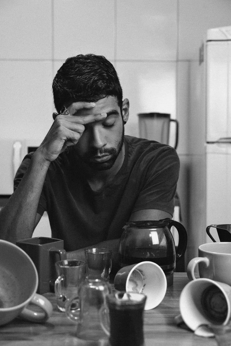 Hombre cansado sentado a la mesa rodeado de tazas vacías de café